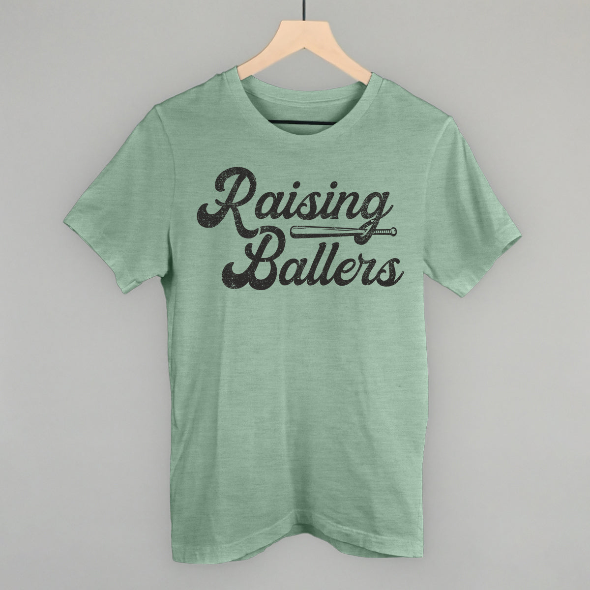 Green t-shirt with 'Raising Ballers' text on a hanger against a gray background