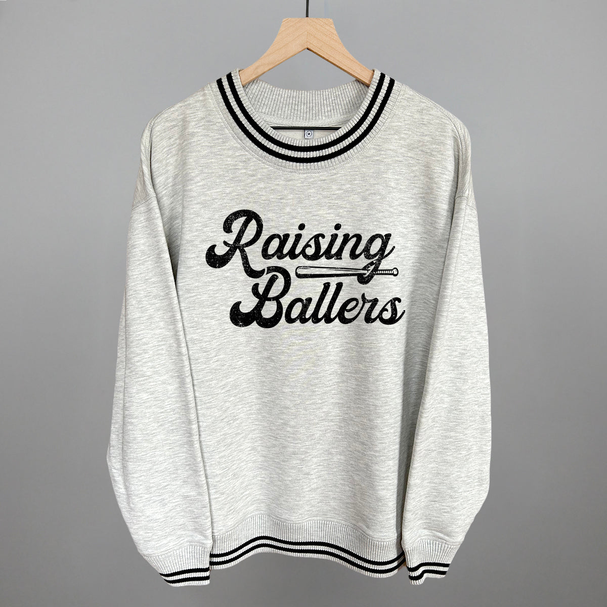 Gray sweatshirt with 'Raising Ballers' text on a hanger against a gray background