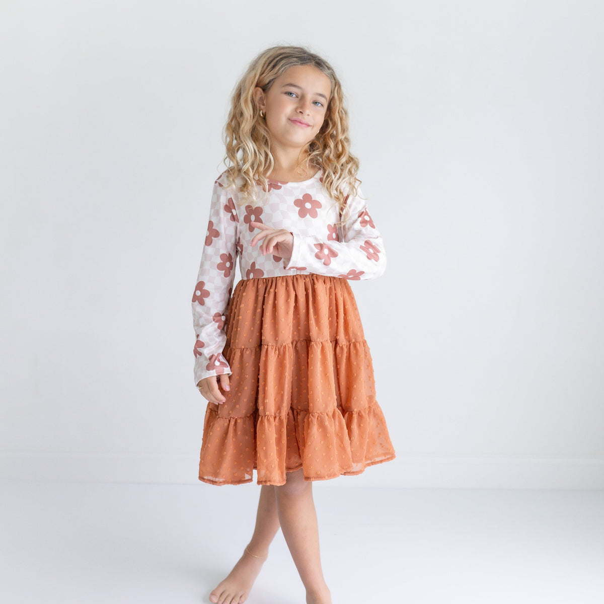 Young girl wearing a floral top and rust-colored skirt on a white background