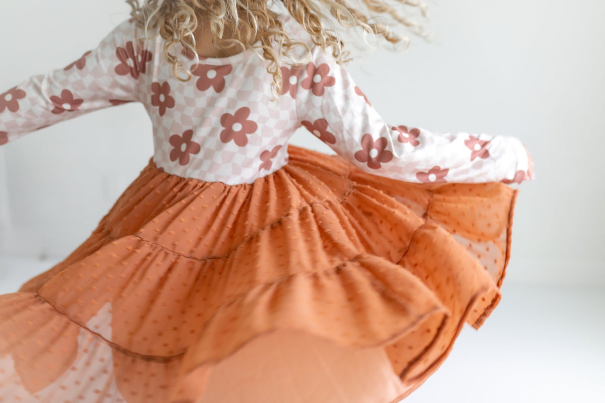 Child wearing a dress with floral top and orange skirt on a white background