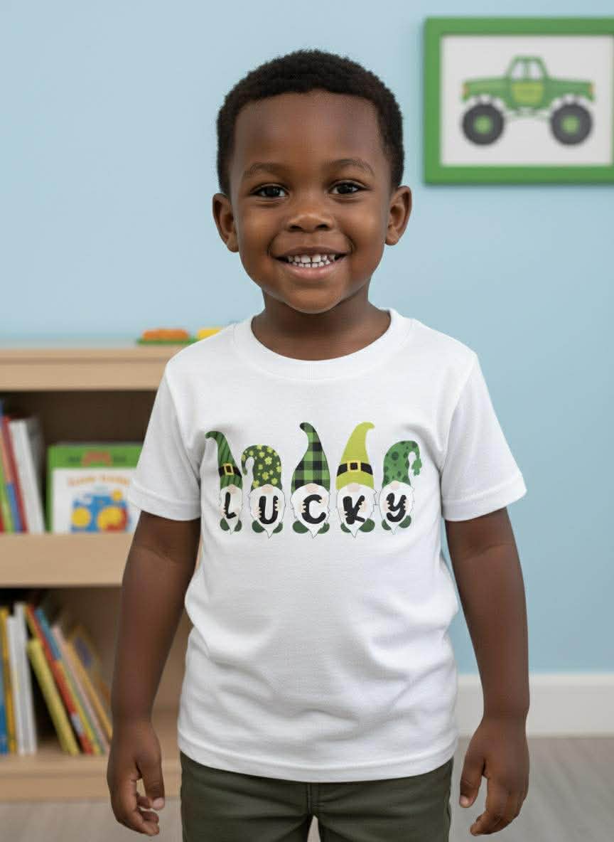 Child wearing a white t-shirt with green gnomes and text, standing in a room with books and a toy truck on the wall.