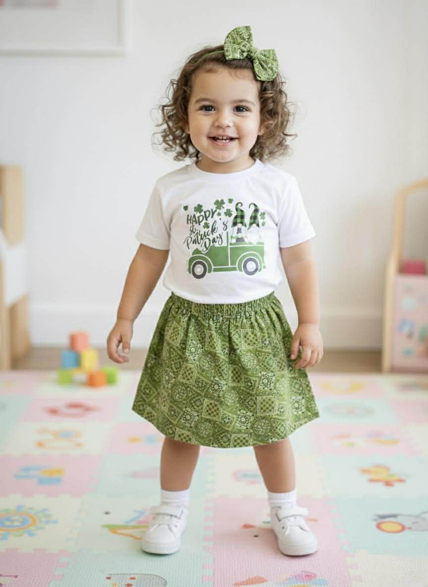 Child wearing a white t-shirt with a green tractor graphic and a green skirt, standing on a colorful play mat.