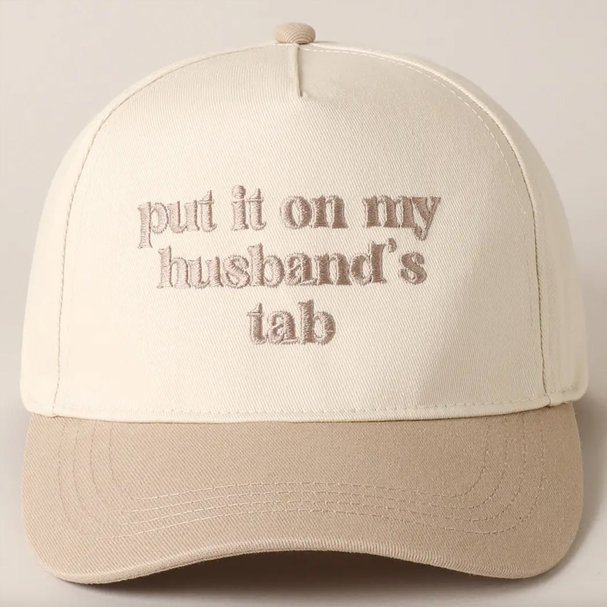 Beige cap with text 'put it on my husband's tab' on a light gray background