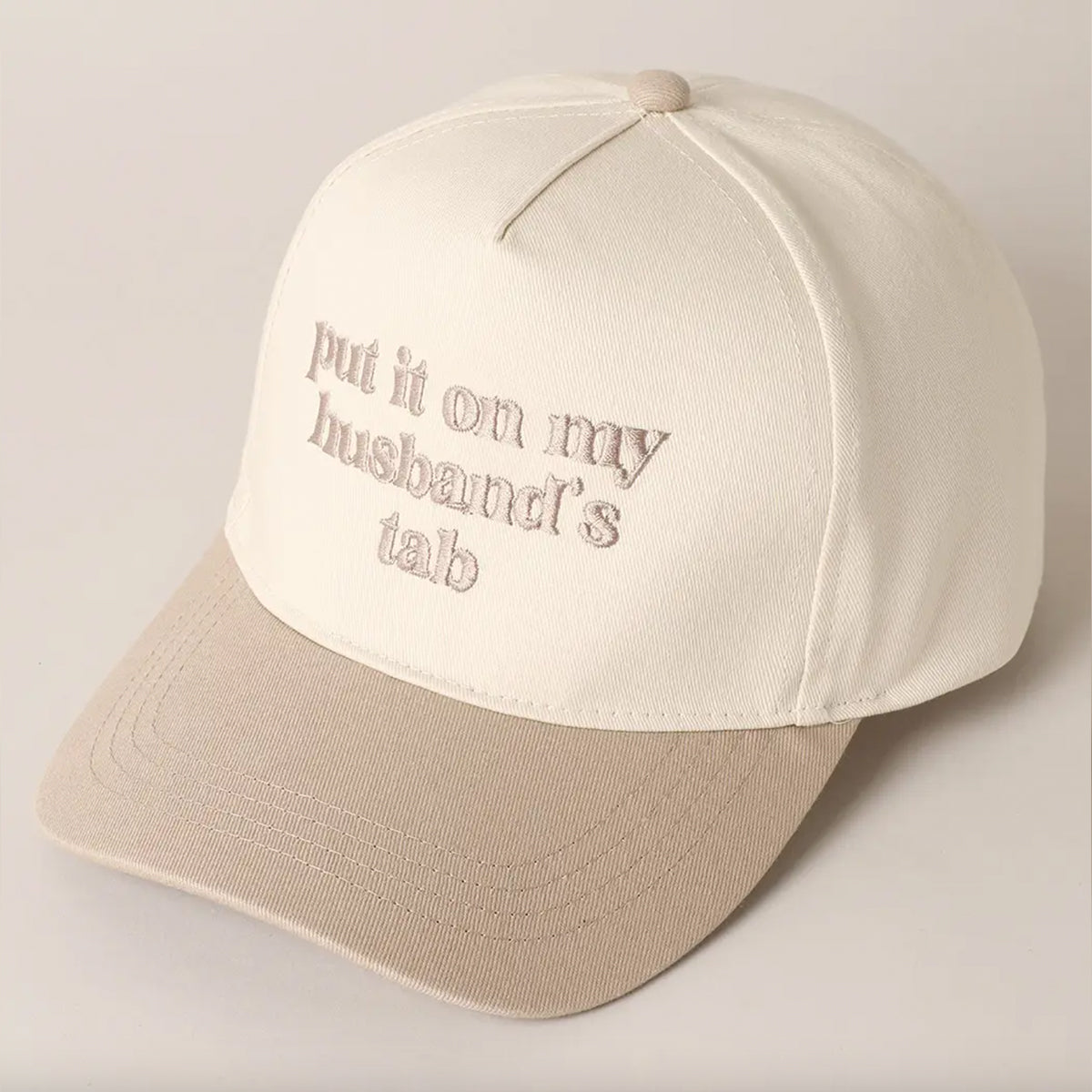 Beige cap with text 'put it on my husband's tab' on a light background